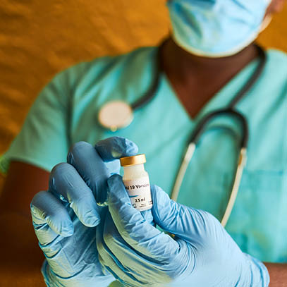 An African doctor holding a covid 19 vaccine vial in his hands while wearing blue surgical gloves and surgical scrubs